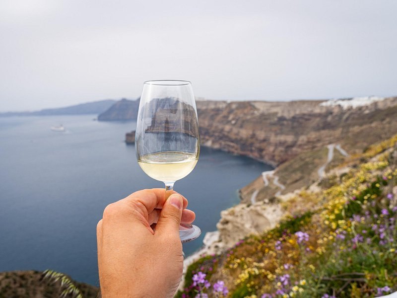 A glass of Assyrtiko held up against the caldera view