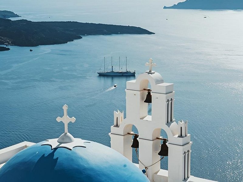 A whitewashed bell tower with the volcano islet of Nea Kameni beyond