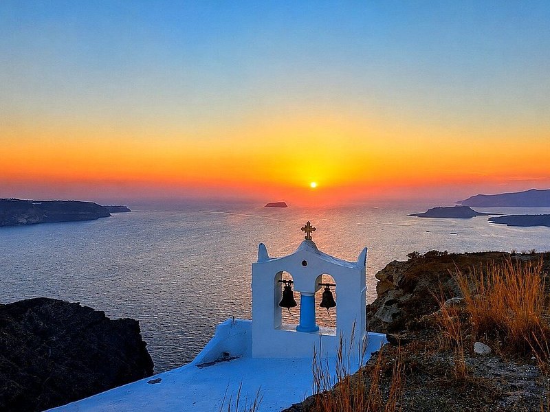 A bell tower silhouetted against the sun setting over the caldera