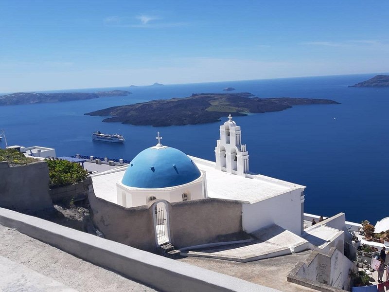 A blue-domed church on the rim with ships anchored in the caldera below