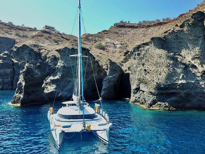 A catamaran anchored in a sheltered cove under the caldera cliffs