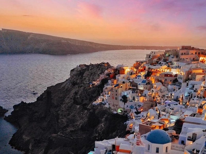 Oia lit at dusk above the dark volcanic rock of the caldera wall