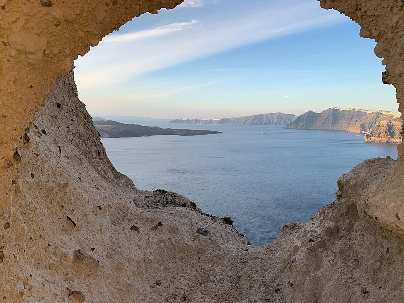 A volcanic rock arch framing the Santorini caldera and Nea Kameni