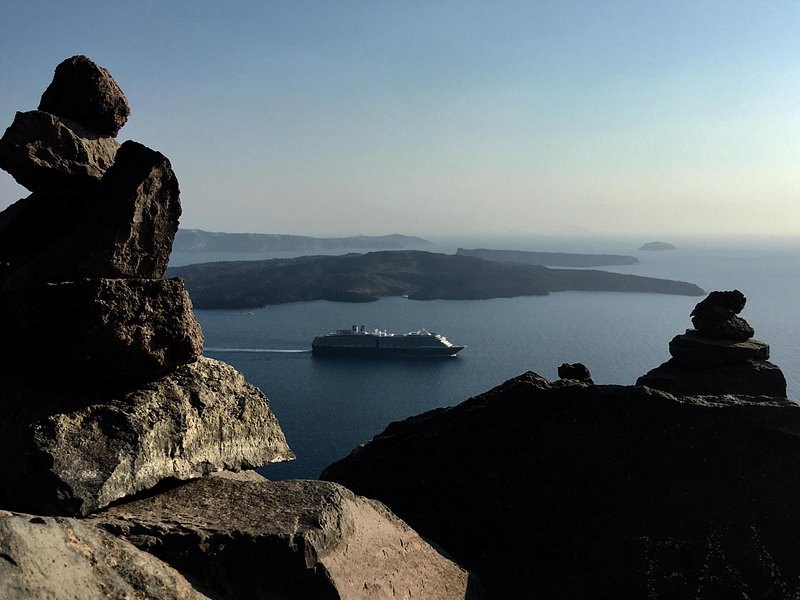 Dark volcanic rock in the foreground and a ship crossing the caldera at dusk